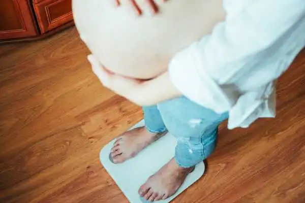 Image of woman weighing herself and experiencing weight gain through pregnancy Hucknall